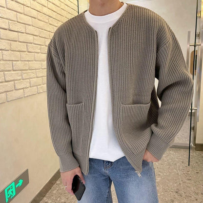 Uomo con cardigan grigio a maglia, tasche frontali, indossa jeans blu e maglietta bianca. Moda casual autunnale, stile urbano moderno.