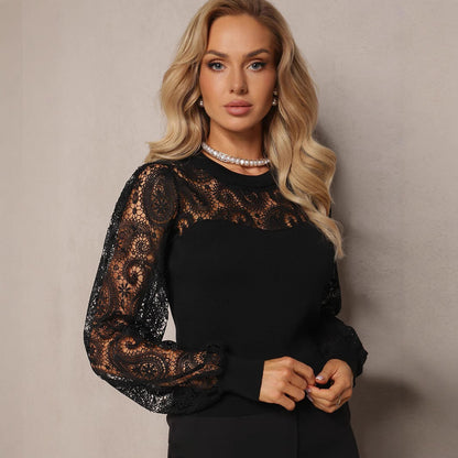 Donna con maglia nera elegante in pizzo, maniche lunghe trasparenti, collana di perle, capelli biondi ondulati, posa su sfondo neutro.