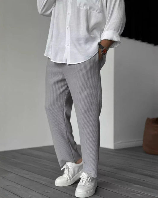 Uomo in camicia bianca e pantaloni grigi a coste, indossa scarpe da ginnastica bianche su pavimento in legno. Moda casual elegante maschile.