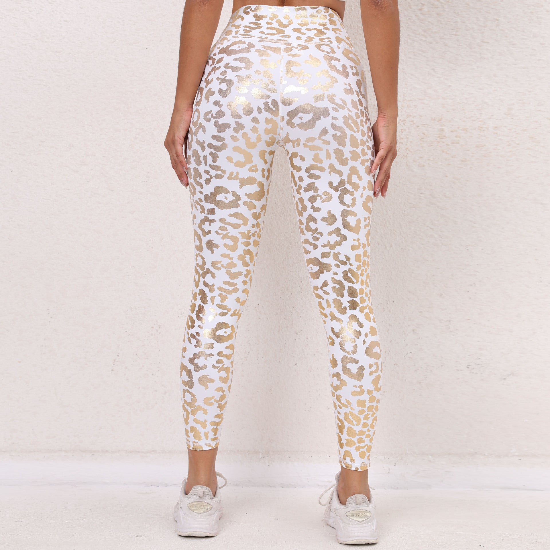 Leggings sportivi donna a vita alta con stampa leopardata bianca e dorata, indossati con scarpe da ginnastica bianche su sfondo neutro.