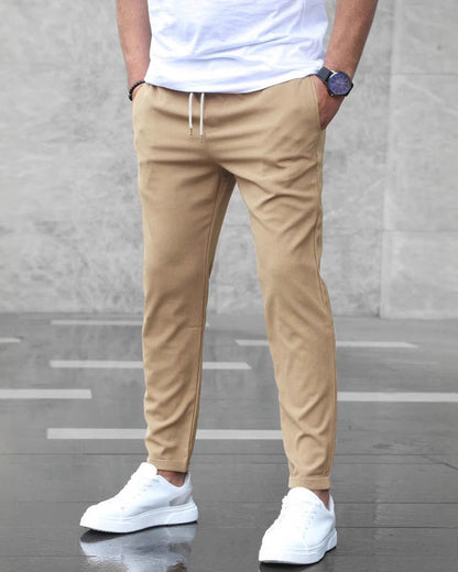 Uomo in pantaloni chino beige e scarpe da ginnastica bianche, camicia bianca, orologio nero. Moda casual maschile, stile urbano elegante.