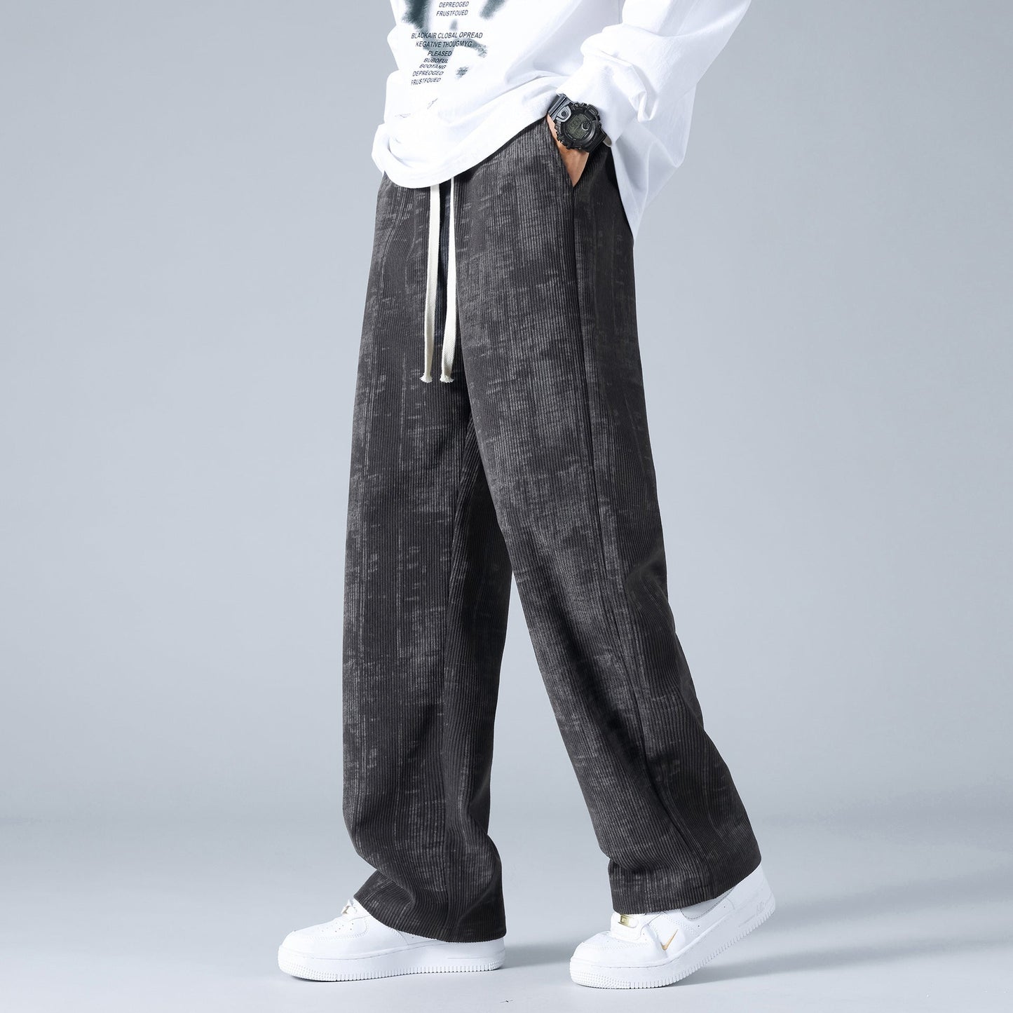 Pantaloni larghi uomo neri, tessuto a trama, abbinati a sneakers bianche e maglia bianca. Stile casual, moda streetwear maschile.