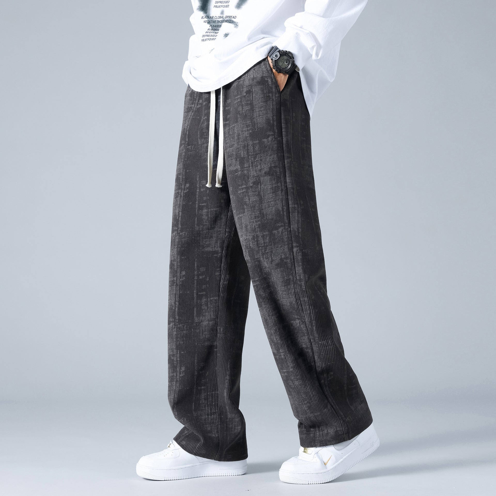 Pantaloni larghi uomo neri, tessuto a trama, abbinati a sneakers bianche e maglia bianca. Stile casual, moda streetwear maschile.