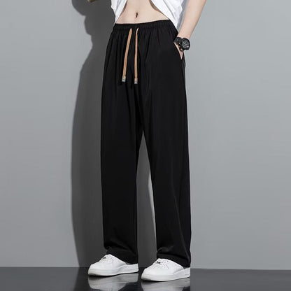 Pantaloni neri larghi da uomo, stile casual, con coulisse marrone, abbinati a scarpe bianche. Moda maschile, abbigliamento comodo.