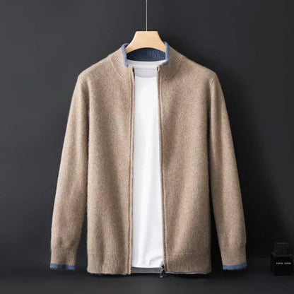 Cardigan beige in cashmere su gruccia, con zip frontale, colletto rialzato e dettagli blu ai polsini. Sfondo nero elegante.