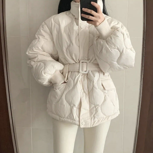 Donna con giacca imbottita bianca, cintura in vita, davanti a uno specchio. Moda invernale, abbigliamento caldo, stile casual chic.