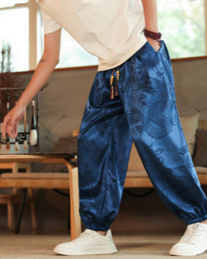 Pantaloni larghi in seta blu con motivo drago, indossati da persona in maglietta bianca e scarpe da ginnastica, stile casual orientale.