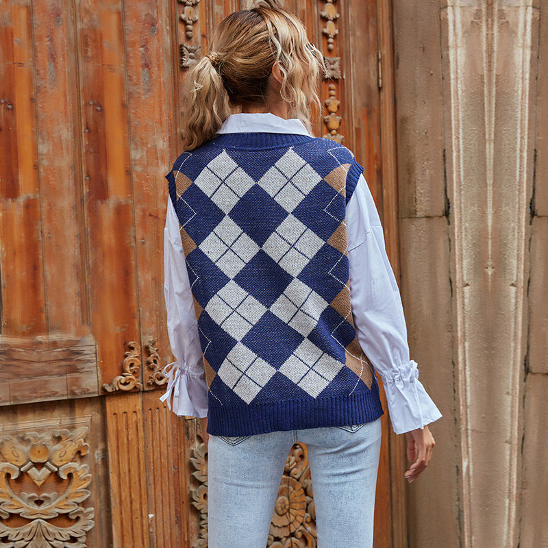 Donna con gilet a rombi blu e bianchi, camicia bianca e jeans chiari, di fronte a una porta in legno intagliato. Moda autunnale casual.