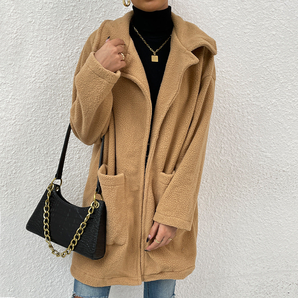 Donna con cappotto teddy beige, maglione nero e jeans, borsa a tracolla nera con catena dorata. Moda autunnale casual chic.