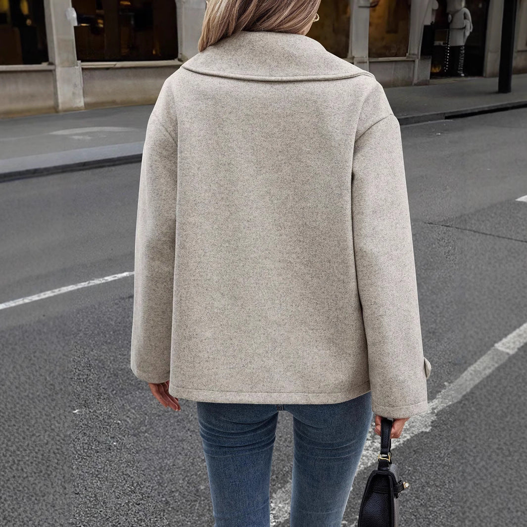 Donna con cappotto beige su strada cittadina, jeans aderenti, borsa nera. Moda autunnale, abbigliamento casual elegante, tendenze street style.