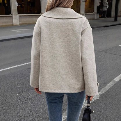 Donna con cappotto beige su strada cittadina, jeans aderenti, borsa nera. Moda autunnale, abbigliamento casual elegante, tendenze street style.