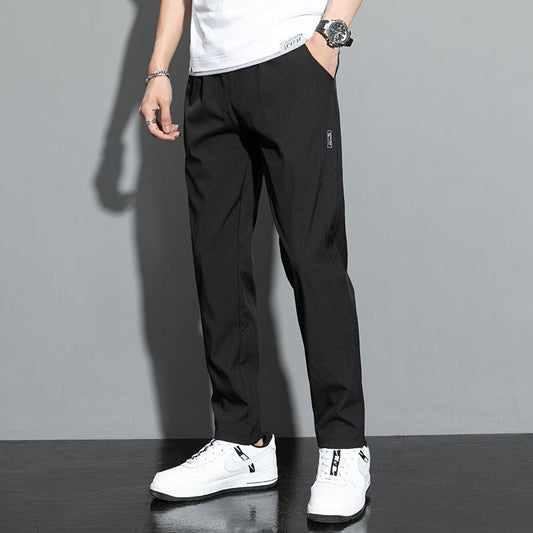 Pantaloni neri eleganti da uomo, abbinati a scarpe da ginnastica bianche, su sfondo grigio. Moda maschile casual, stile moderno.