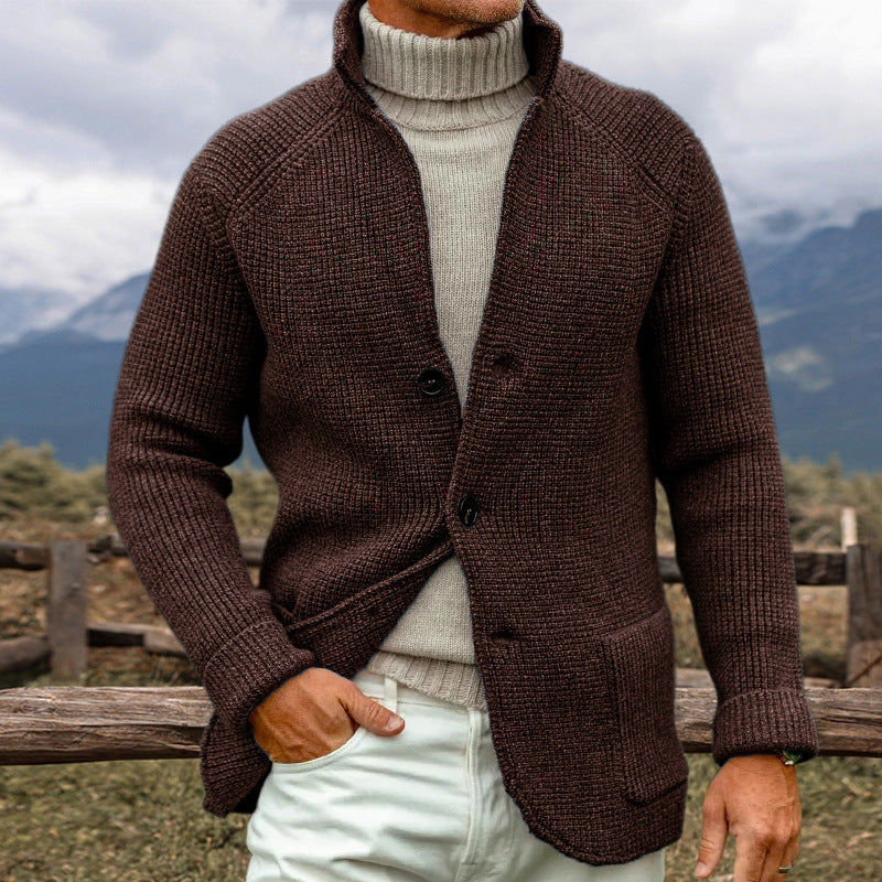 Uomo con maglione marrone a maglia grossa e dolcevita beige, in un paesaggio montano. Moda autunnale, abbigliamento caldo e casual.