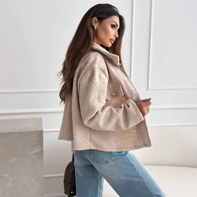 Donna con giacca in lana beige e jeans, posa elegante in interni moderni. Moda autunnale, stile casual chic, tendenze abbigliamento femminile.