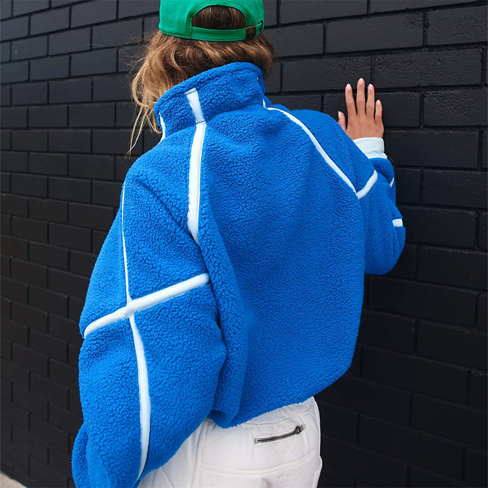 Donna con giacca in pile blu e cappello verde, appoggiata a muro nero. Moda autunno, abbigliamento casual, stile urbano.