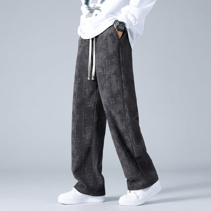 Pantaloni larghi neri con motivo astratto, indossati con maglietta bianca e scarpe da ginnastica bianche. Stile casual moderno maschile.
