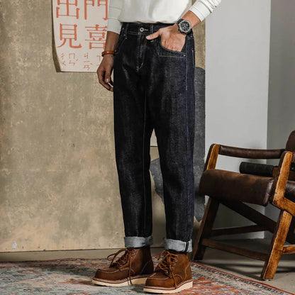 Uomo in jeans scuri e stivali marroni, in piedi accanto a una sedia di legno. Moda casual maschile, abbigliamento autunnale.