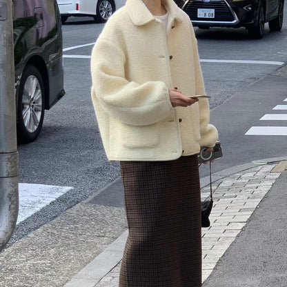 Donna con cappotto oversize bianco crema e gonna a quadri marrone su strada cittadina. Moda autunnale, stile urbano, abbigliamento casual.