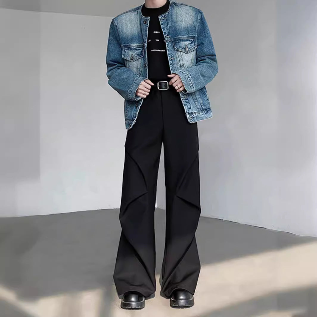 Giacca di jeans blu su maglietta nera, pantaloni neri larghi con pieghe, cintura nera, scarpe nere. Moda casual uomo, stile urbano moderno.