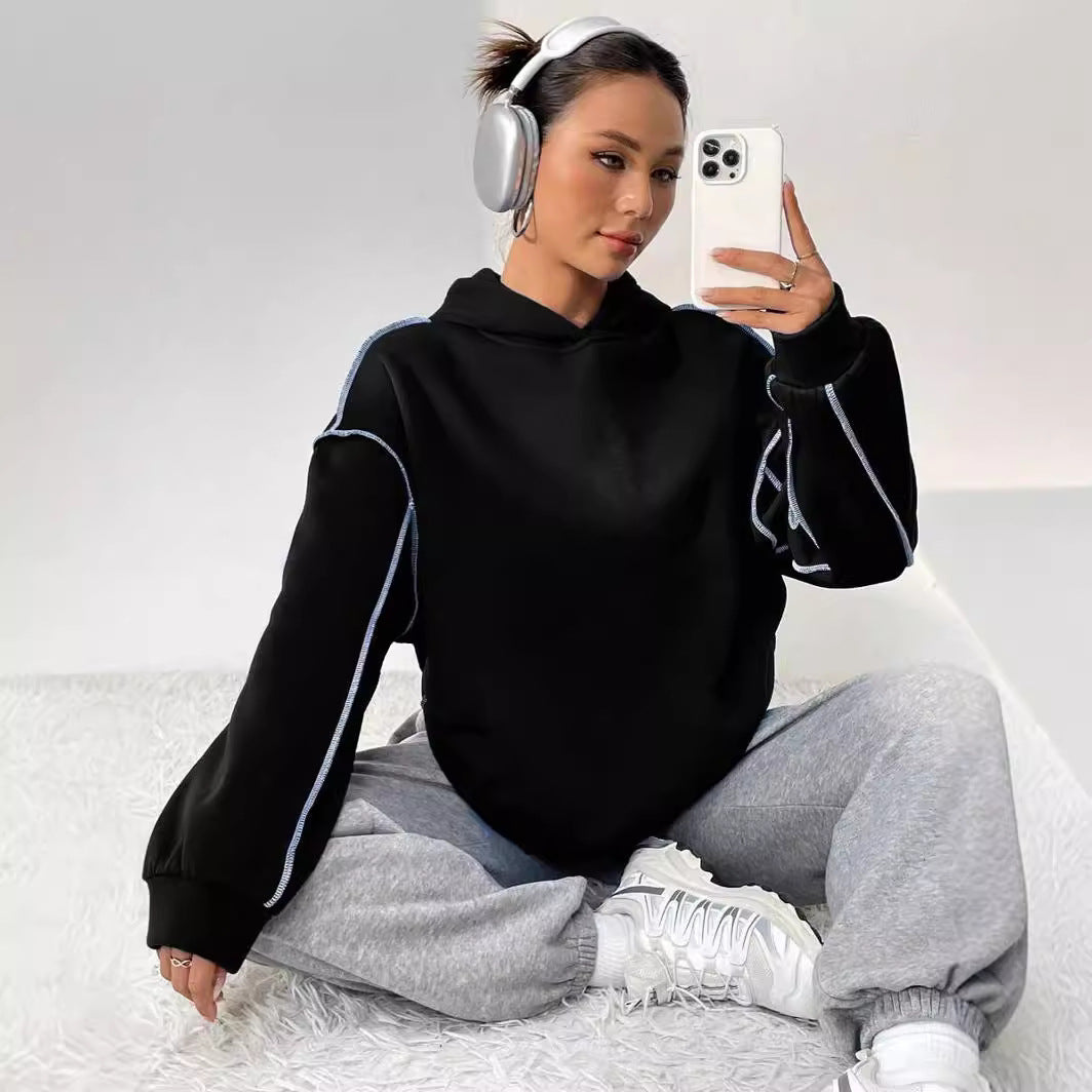 Donna con cuffie wireless, felpa nera e pantaloni grigi, scatta un selfie con smartphone. Look casual e moderno, moda streetwear.