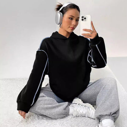 Donna con cuffie wireless, felpa nera e pantaloni grigi, scatta un selfie con smartphone. Look casual e moderno, moda streetwear.