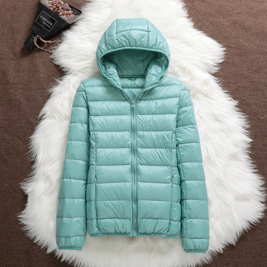 Giacca invernale verde menta con cappuccio, imbottita e trapuntata, su sfondo di pelliccia bianca. Moda donna, abbigliamento caldo e trendy.