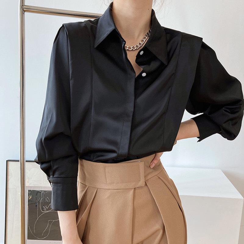 Camicia nera elegante in raso con colletto classico e maniche lunghe, abbinata a pantaloni beige a vita alta. Look moda donna sofisticato.