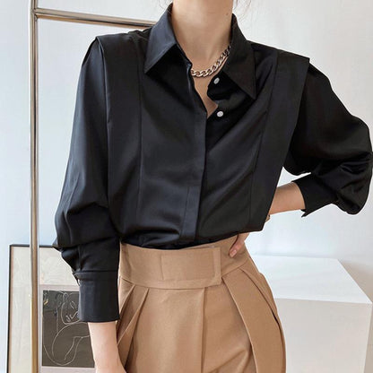 Camicia nera elegante in raso con colletto classico e maniche lunghe, abbinata a pantaloni beige a vita alta. Look moda donna sofisticato.