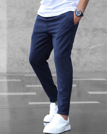 Uomo con pantaloni blu eleganti e scarpe bianche su sfondo grigio. Stile casual chic, moda maschile, abbigliamento moderno.