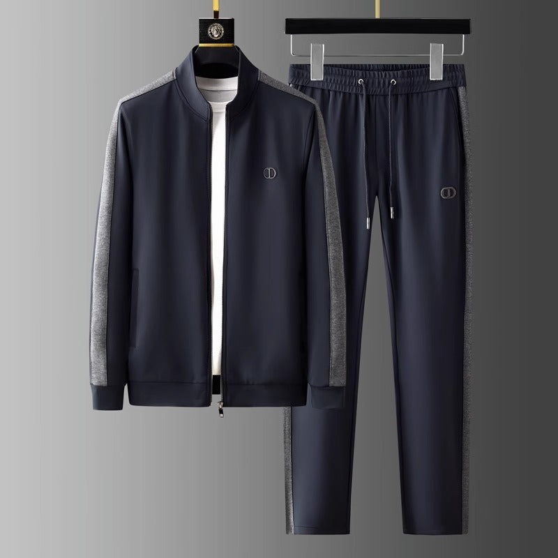 Tuta sportiva uomo blu scuro con giacca e pantaloni, dettagli grigi, logo discreto, appesa su gruccia. Abbigliamento casual elegante.