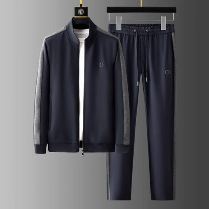 Tuta sportiva uomo blu scuro con giacca e pantaloni, dettagli grigi, logo discreto, appesa su gruccia. Abbigliamento casual elegante.