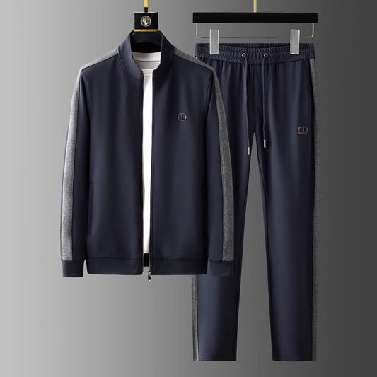 Tuta sportiva uomo blu scuro con giacca e pantaloni, dettagli grigi, logo discreto, appesa su gruccia. Abbigliamento casual elegante.
