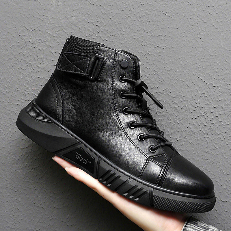 Scarpa nera alta in pelle con lacci e cinturino alla caviglia, suola robusta, tenuta in mano su sfondo grigio. Scarpe moda uomo, calzature eleganti.