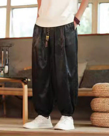 Pantaloni larghi neri in seta con motivo floreale, indossati con scarpe bianche. Stile casual, moda uomo, abbigliamento confortevole.