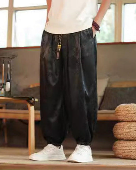 Pantaloni larghi neri in seta con motivo floreale, indossati con scarpe bianche. Stile casual, moda uomo, abbigliamento confortevole.