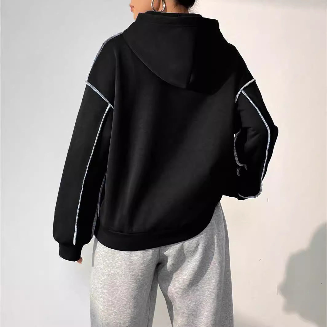 Donna di spalle con felpa nera con cappuccio e pantaloni grigi. Moda casual, abbigliamento sportivo, stile urbano.