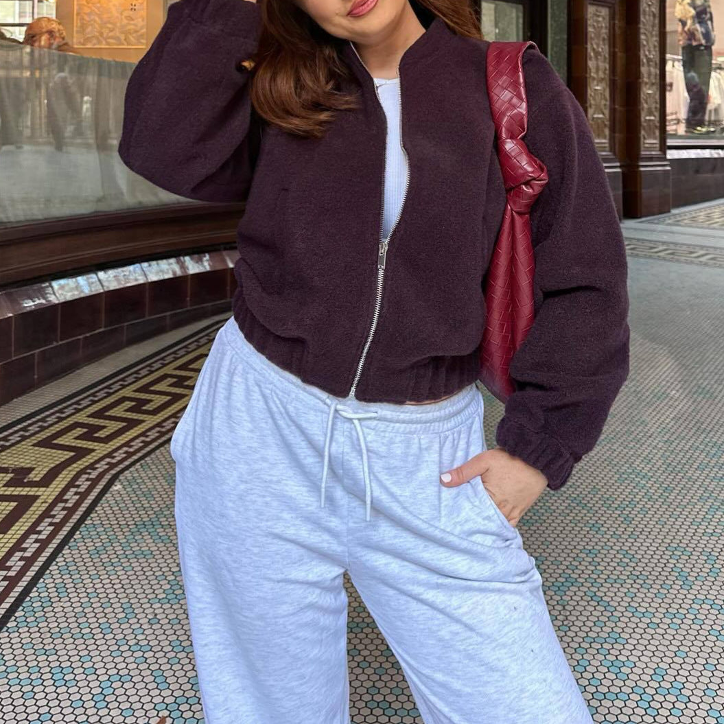 Giacca in pile marrone scuro con zip, abbinata a pantaloni sportivi grigi e borsa trapuntata rossa. Moda casual autunnale in città.