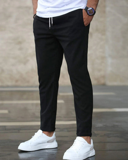 Uomo con pantaloni neri casual e scarpe da ginnastica bianche, sfondo urbano. Moda maschile, abbigliamento casual, stile moderno.