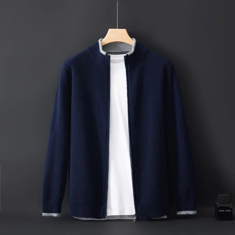 Cardigan blu scuro da uomo su sfondo nero, appeso a una gruccia, con zip aperta e maglietta bianca sotto. Moda maschile elegante e casual.