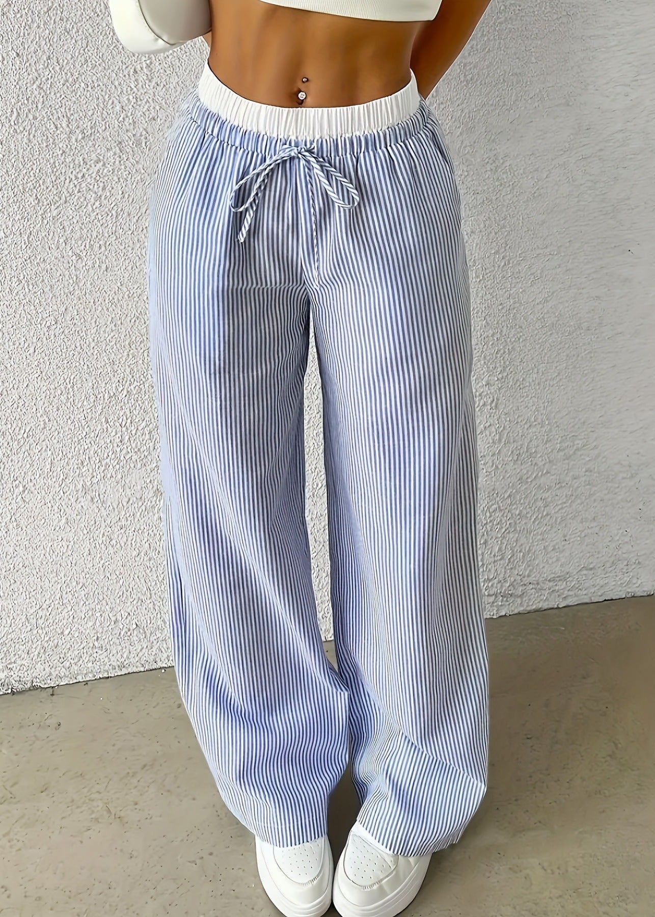 Pantaloni a righe bianche e blu, larghi e a vita alta, con coulisse. Indossati con top bianco e sneakers bianche. Moda casual estiva.