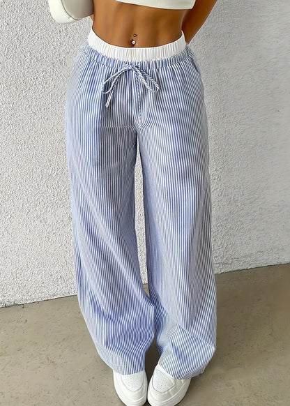 Pantaloni a righe bianche e blu, larghi e a vita alta, con coulisse. Indossati con top bianco e sneakers bianche. Moda casual estiva.