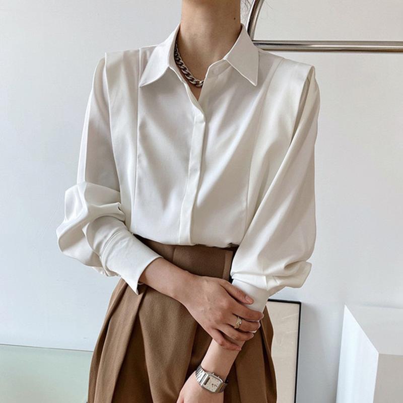 Camicia bianca elegante da donna con colletto classico e maniche lunghe, abbinata a pantaloni marroni. Stile formale e moderno.