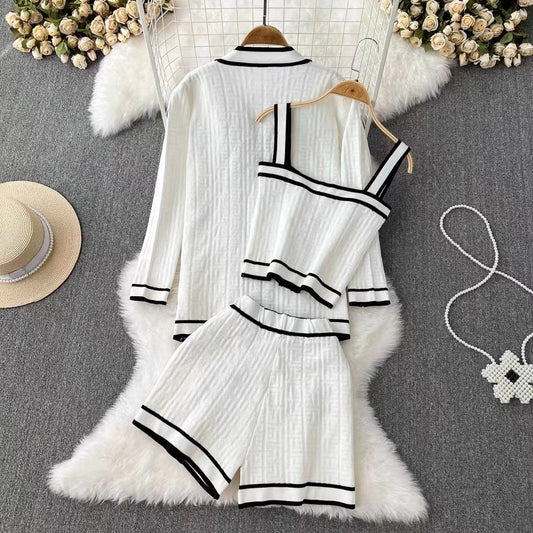 Completo pigiama donna bianco a righe nere, composto da giacca, top e pantaloncini, su tappeto peloso bianco, con cappello e borsa a fiori.