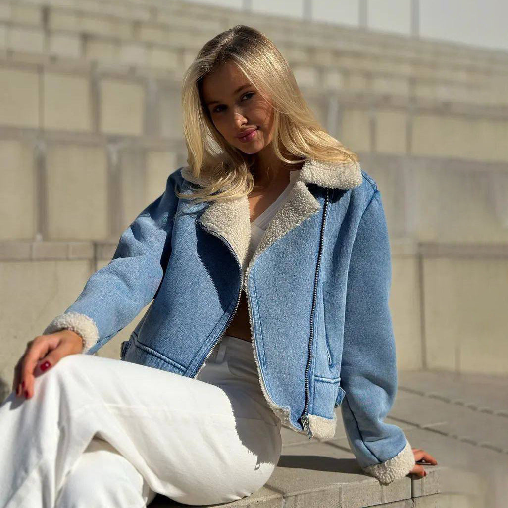 Donna seduta su gradini indossa giacca di jeans con interno in pelliccia sintetica e pantaloni bianchi. Moda autunnale casual, look trendy.