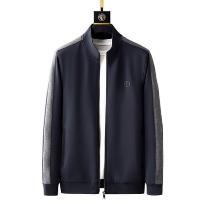 Giacca sportiva uomo blu scuro con maniche grigie, chiusura zip, logo sul petto. Moda casual, abbigliamento autunnale, stile elegante.