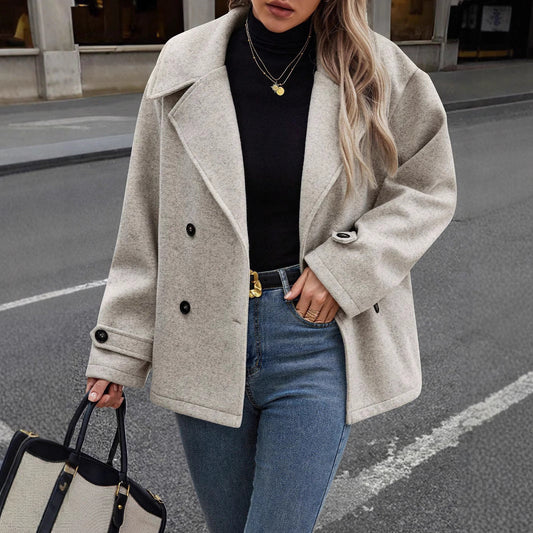 Donna con cappotto beige elegante, maglione nero e jeans, tiene una borsa nera. Moda autunnale, abbigliamento casual chic, strada cittadina.