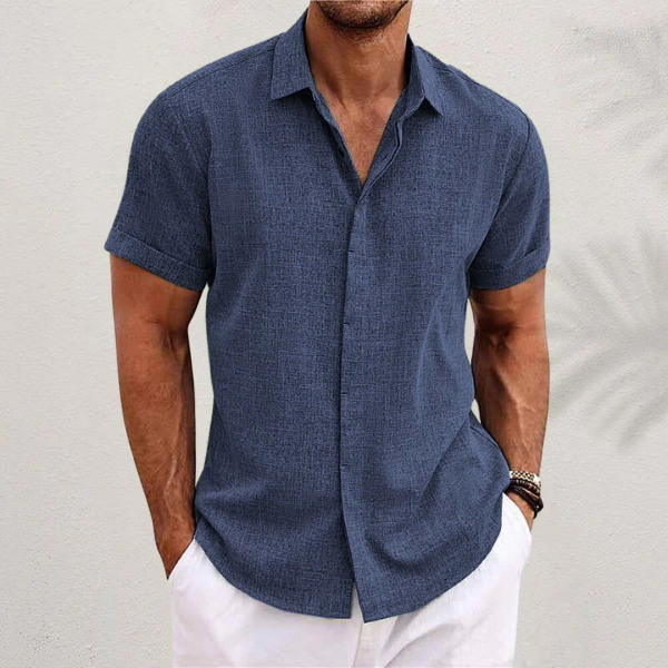 Camicia estiva uomo blu scuro, maniche corte, tessuto leggero, abbinata a pantaloni bianchi. Look casual ed elegante per la moda maschile estiva.