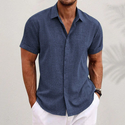 Camicia estiva uomo blu scuro, maniche corte, tessuto leggero, abbinata a pantaloni bianchi. Look casual ed elegante per la moda maschile estiva.