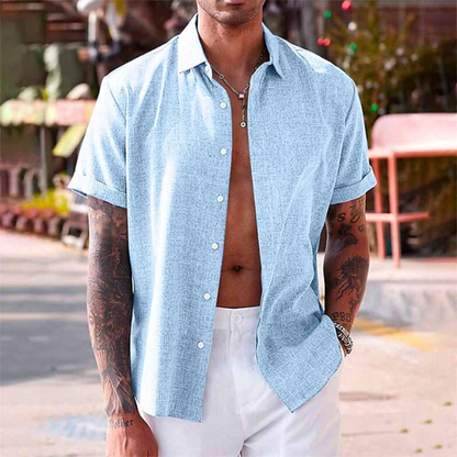 Uomo con camicia estiva azzurra a maniche corte, aperta sul petto, in strada soleggiata. Stile casual, moda maschile estiva.