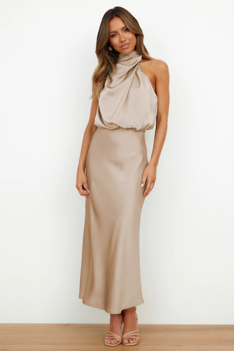 Donna in abito lungo beige elegante, senza maniche, con scollo drappeggiato. Moda femminile, abbigliamento da sera, stile sofisticato.